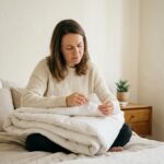 Femme examinant l'étiquette d'une couette blanche épaisse assise sur un lit aux draps en lin neutres