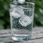 Gouttelettes de condensation sur un verre d'eau froide posé sur une table en bois, illustrant le phénomène de condensation de la vapeur d'eau