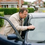 Homme examinant une fissure sur le pare-brise de sa voiture
