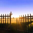 the sun is setting behind a fence in a field