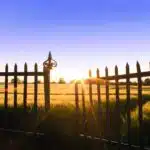 the sun is setting behind a fence in a field