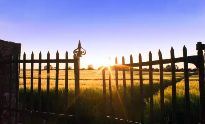 the sun is setting behind a fence in a field